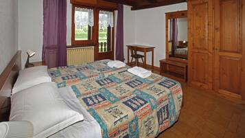 Un dormitorio con una cama grande, un armario de madera, una mesita pequeña y una ventana con cortinas.
