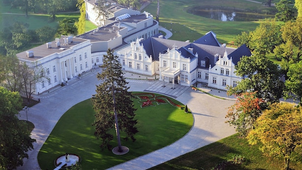 A large, white, historic building with a symmetrical facade, a central courtyard, and a golf course in the background. - Palac Romantyczny (Lysomice)