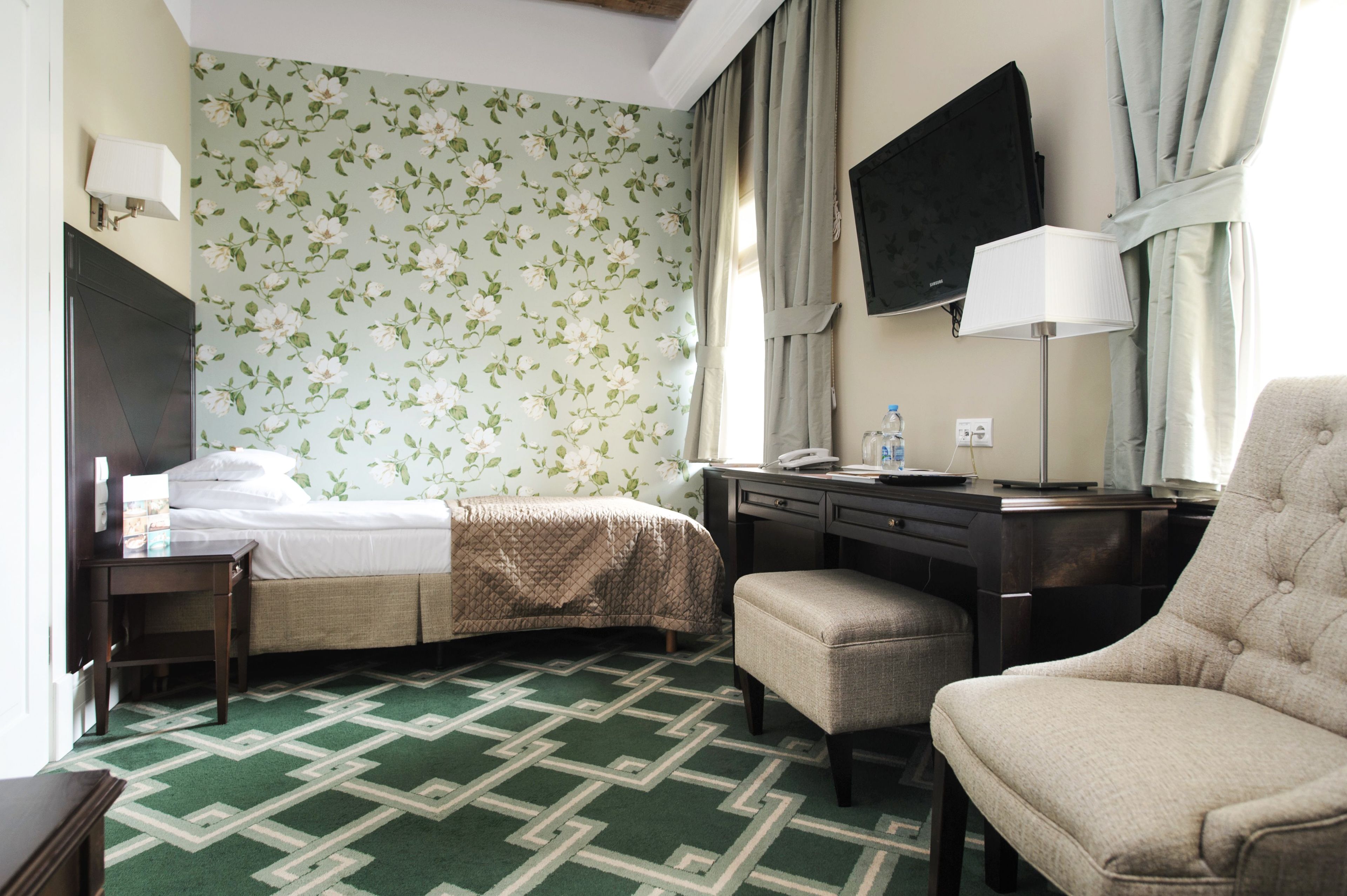 A hotel room with a bed, a desk, a chair, a TV, and a patterned wall.