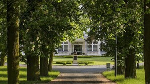 A pathway leading to a building with a statue in the center, surrounded by trees. - Palac Romantyczny (Lysomice)