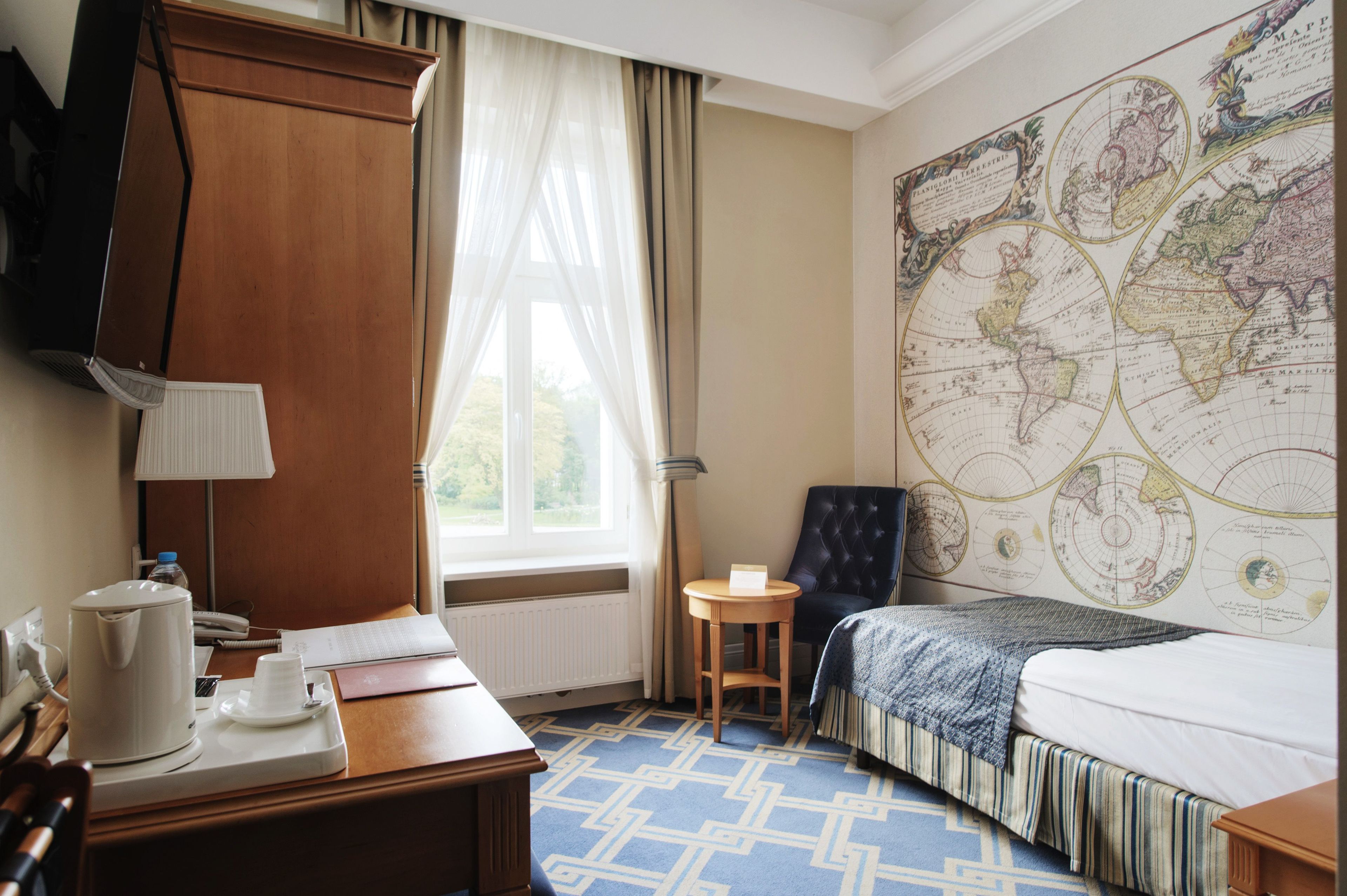 Ein Hotelzimmer mit einer großen Weltkarte an der Wand, einem Bett, einem Schreibtisch mit Kaffeemaschine und einem Sessel.