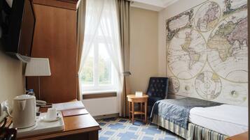 Ein Hotelzimmer mit einer großen Weltkarte an der Wand, einem Bett, einem Schreibtisch mit Kaffeemaschine und einem Sessel.