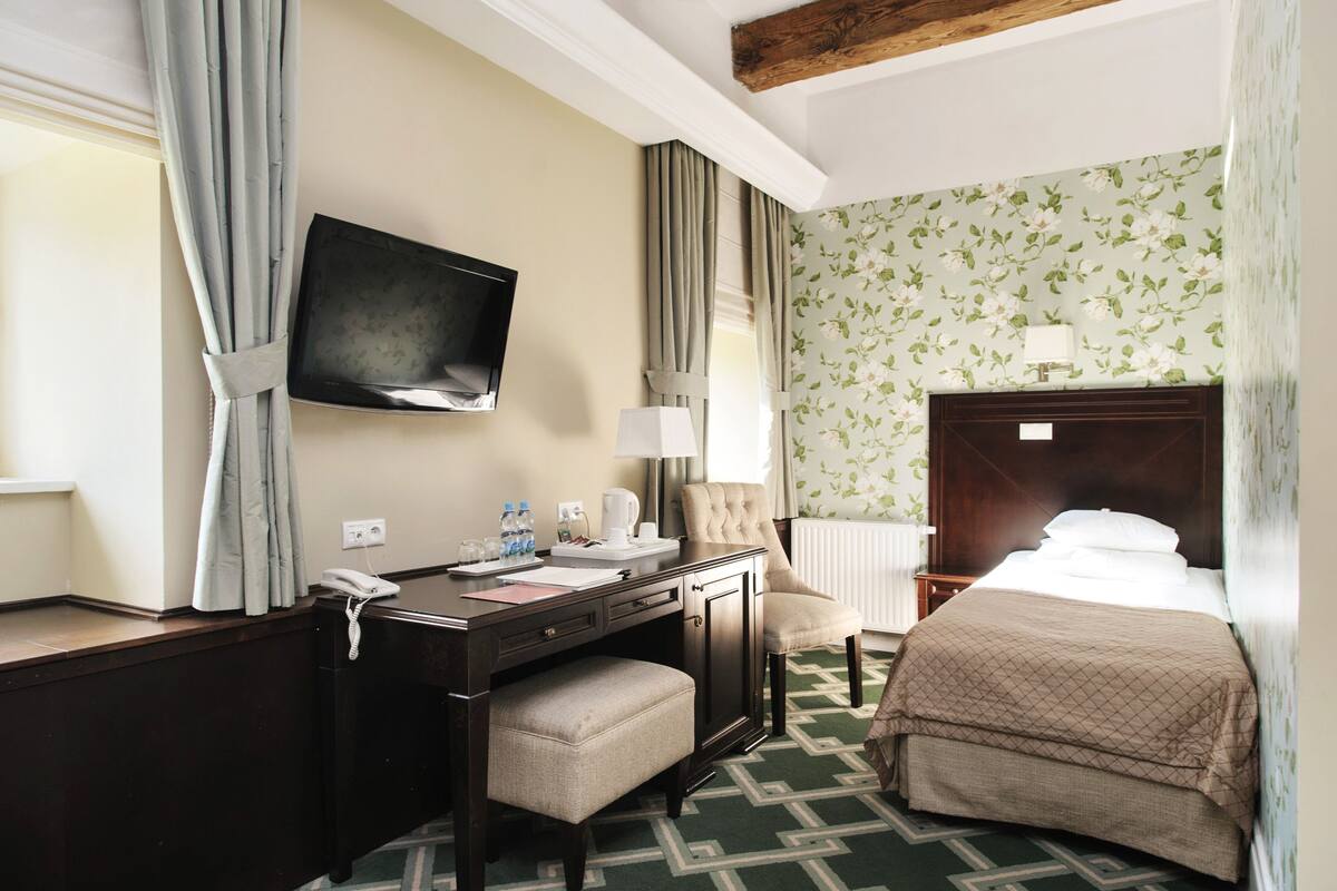 A hotel room with a bed, desk, chair, and a television on the wall.
