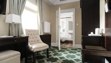 Habitación de hotel con alfombra verde estampada, un sillón capitonado, un escritorio con lámpara y un armario.