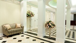 A lobby with a checkered floor, a striped sofa, and two floral arrangements. - Palac Romantyczny (Lysomice)