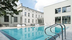 A swimming pool with a glass barrier and metal handrails, surrounded by a modern building with large windows and a white facade. - Palac Romantyczny (Lysomice)