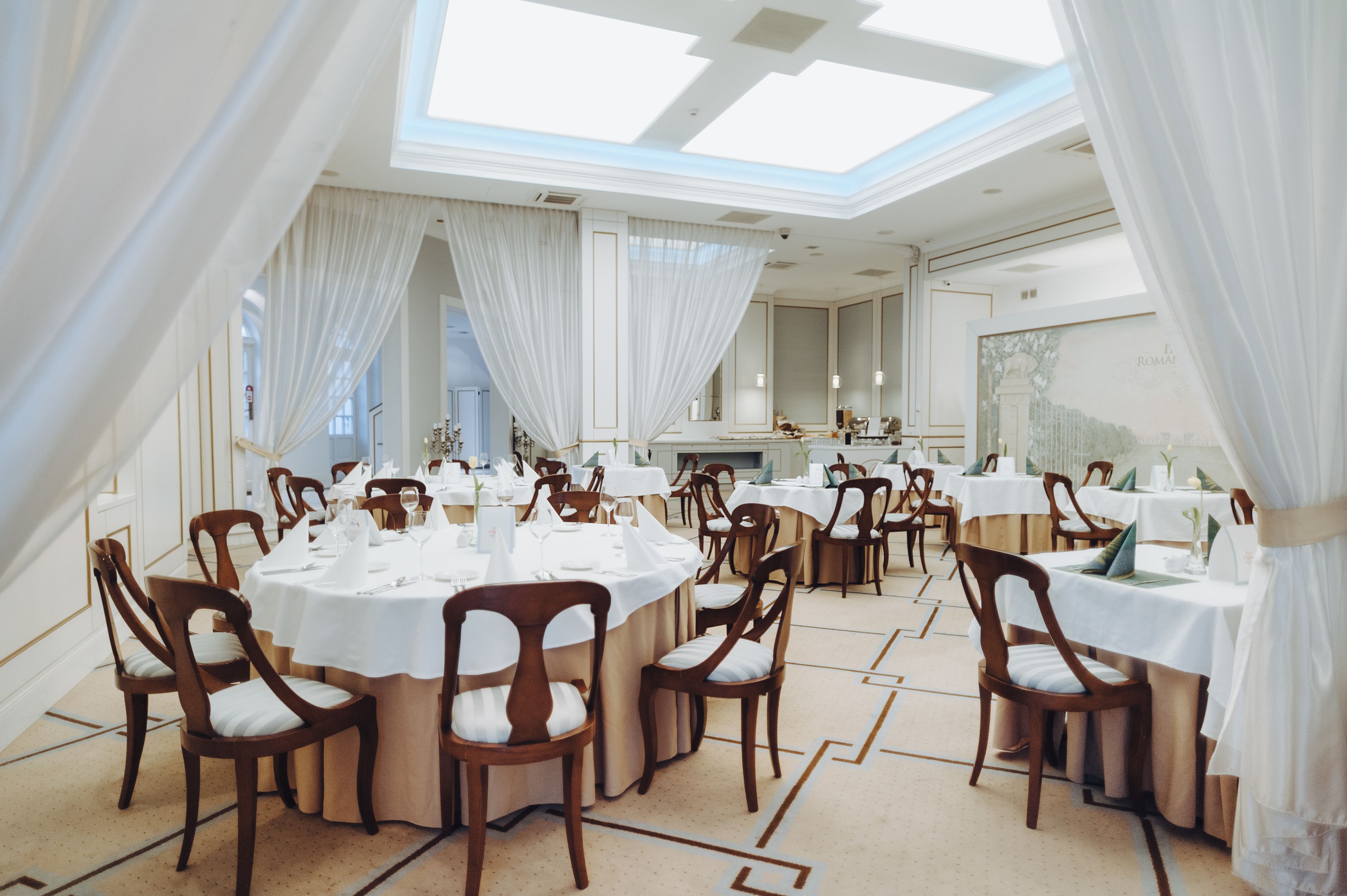 Un comedor amplio con mesas redondas y sillas de madera, ventanas grandes y un techo alto con luz natural.