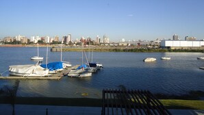 Una marina con varias embarcaciones amarradas, un horizonte urbano al fondo y cielo despejado.