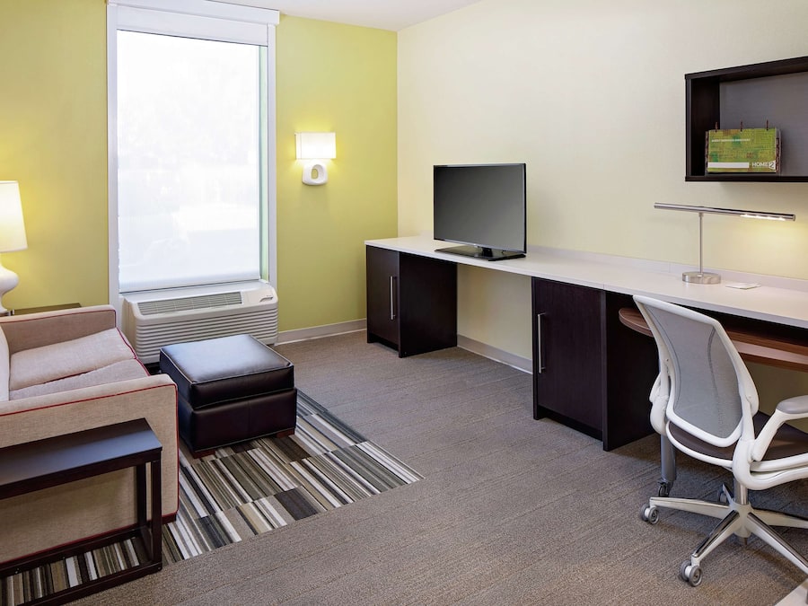 Ein modernes Hotelzimmer mit einer Sitzecke, einem Schreibtisch mit Computer, einem Fernseher und einer Lampe.