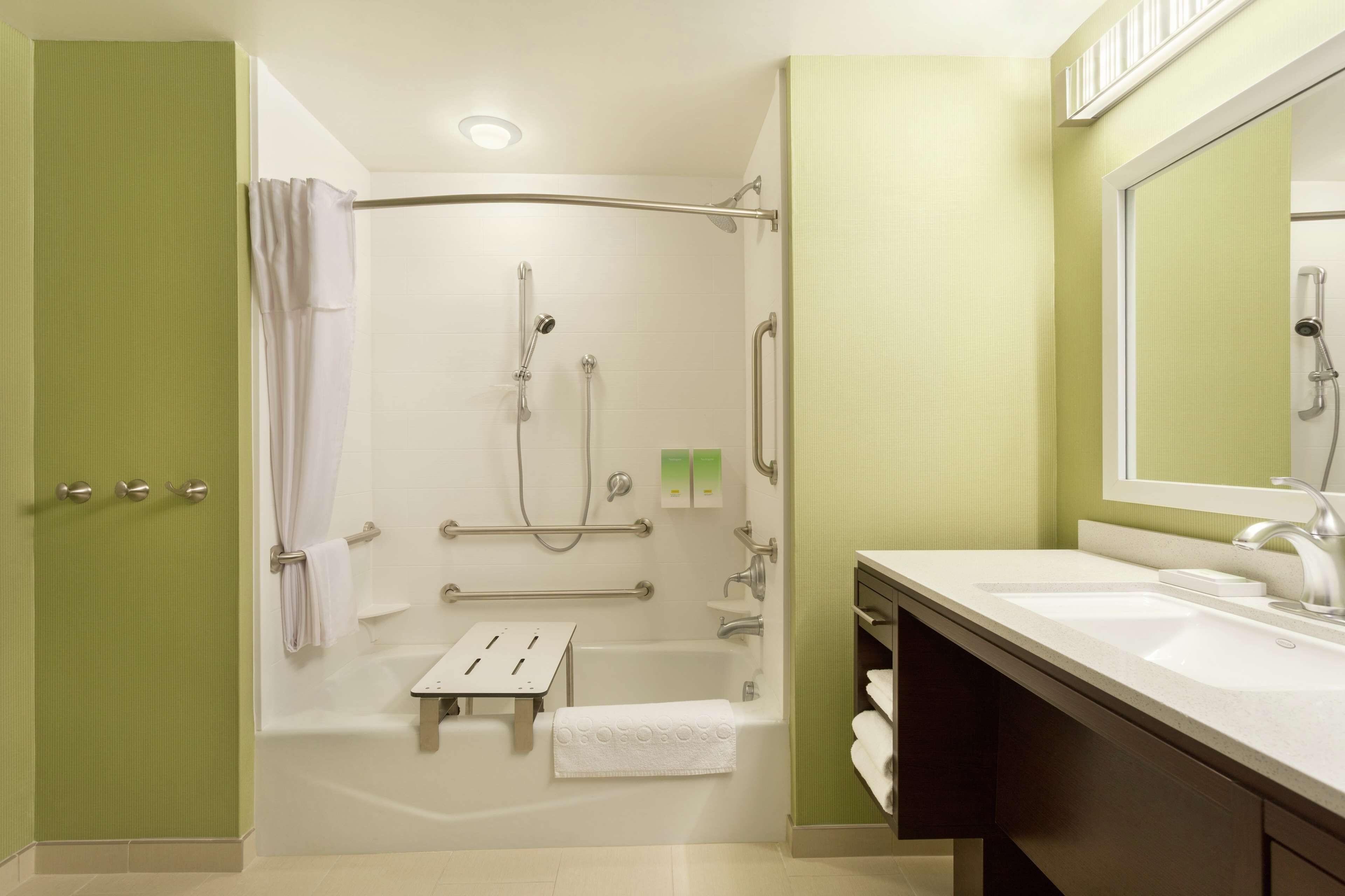 Un baño moderno con ducha, barras de apoyo, bañera y tocador con lavabo.