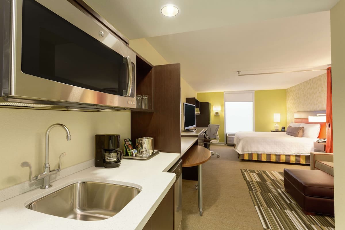 A hotel room with a kitchenette, a bed, a desk, and a bathroom.