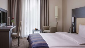 A hotel room with a bed, a desk with a computer, a chair, a small table with a vase of flowers, and a lamp. - IntercityHotel Ingolstadt (Ingolstadt)