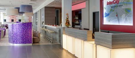 Un espace d’accueil moderne, typique d’un hôtel, avec un bar, des sièges et une grande carte affichée.