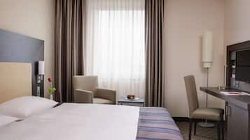 Ein Hotelzimmer mit einem Bett, einem Schreibtisch, einem Sessel, einem kleinen Tisch mit Früchten und einem Fernseher.