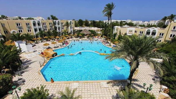 A large swimming pool surrounded by palm trees and sun loungers, with a view of hotel buildings in the background. - Joya Paradise (Djerba Midun)