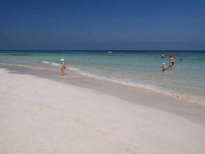 A beach with clear water and a boat in the distance. - Joya Paradise (Djerba Midun)