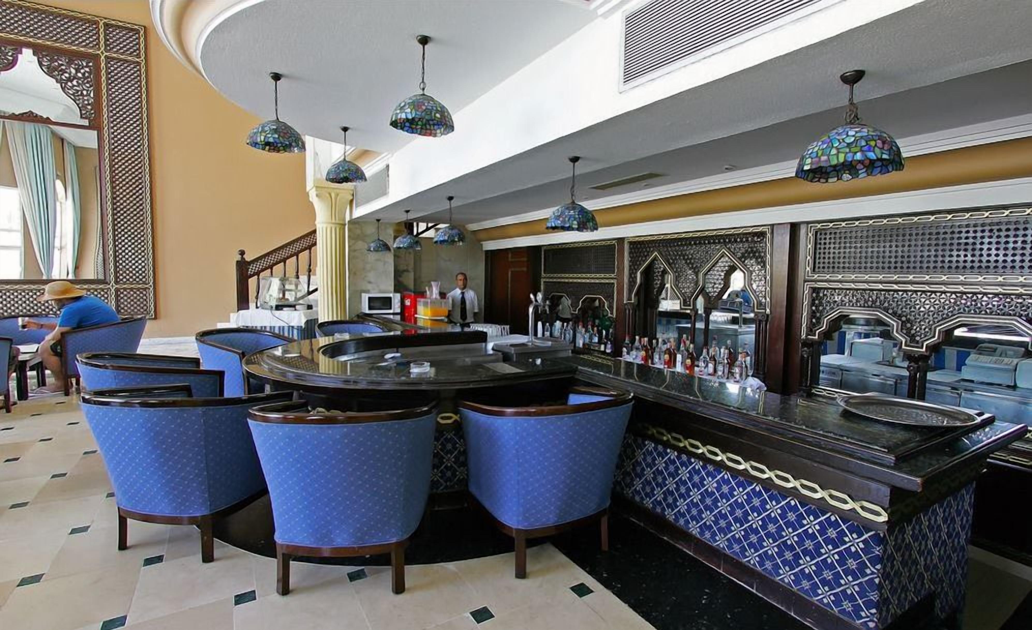 Eine Bar mit blauen Sitzgelegenheiten, einer zentralen Bar und dekorativen Pendelleuchten.