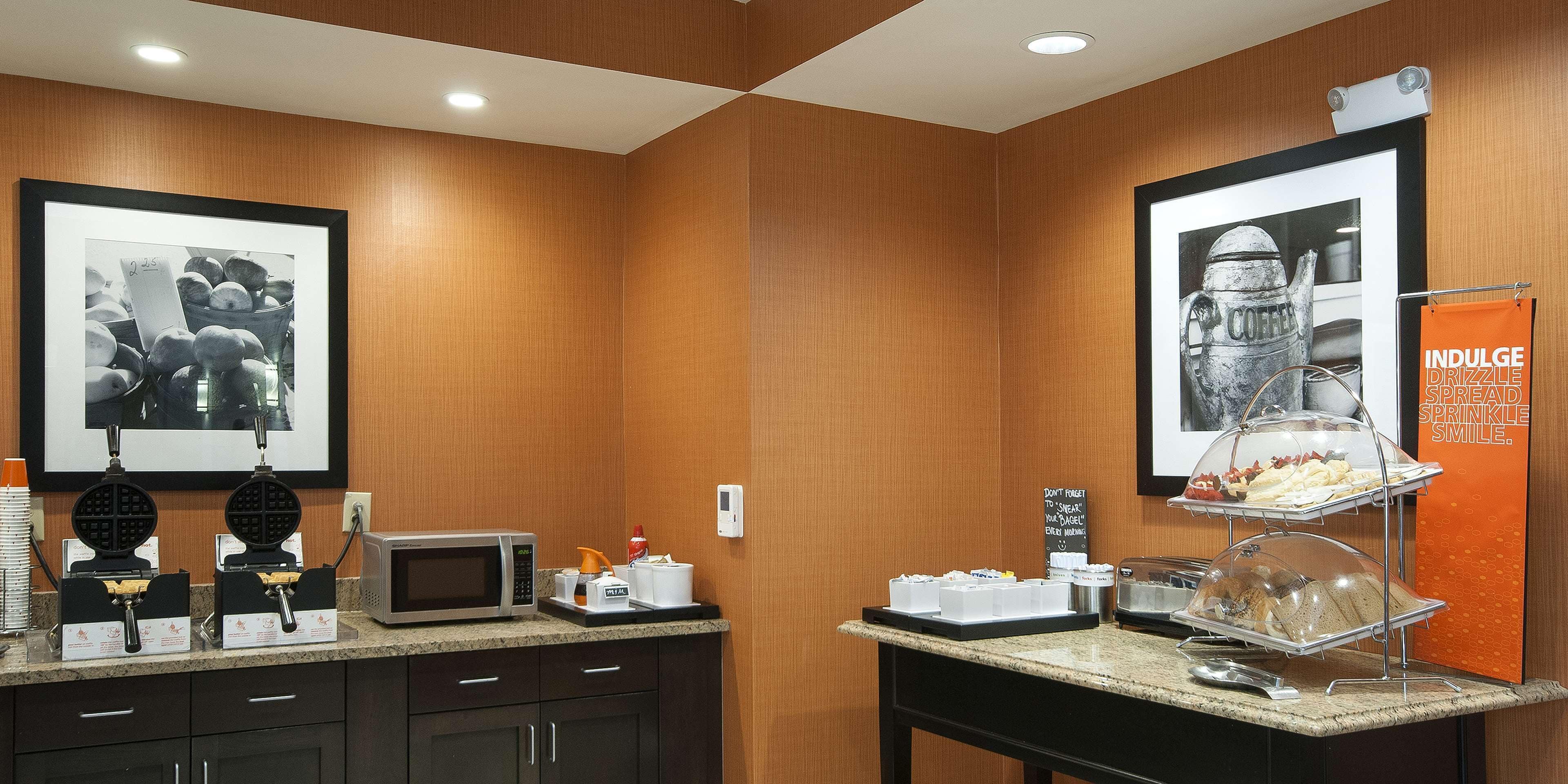 Uma cozinha de hotel com micro-ondas, máquina de waffles e espaço para café.