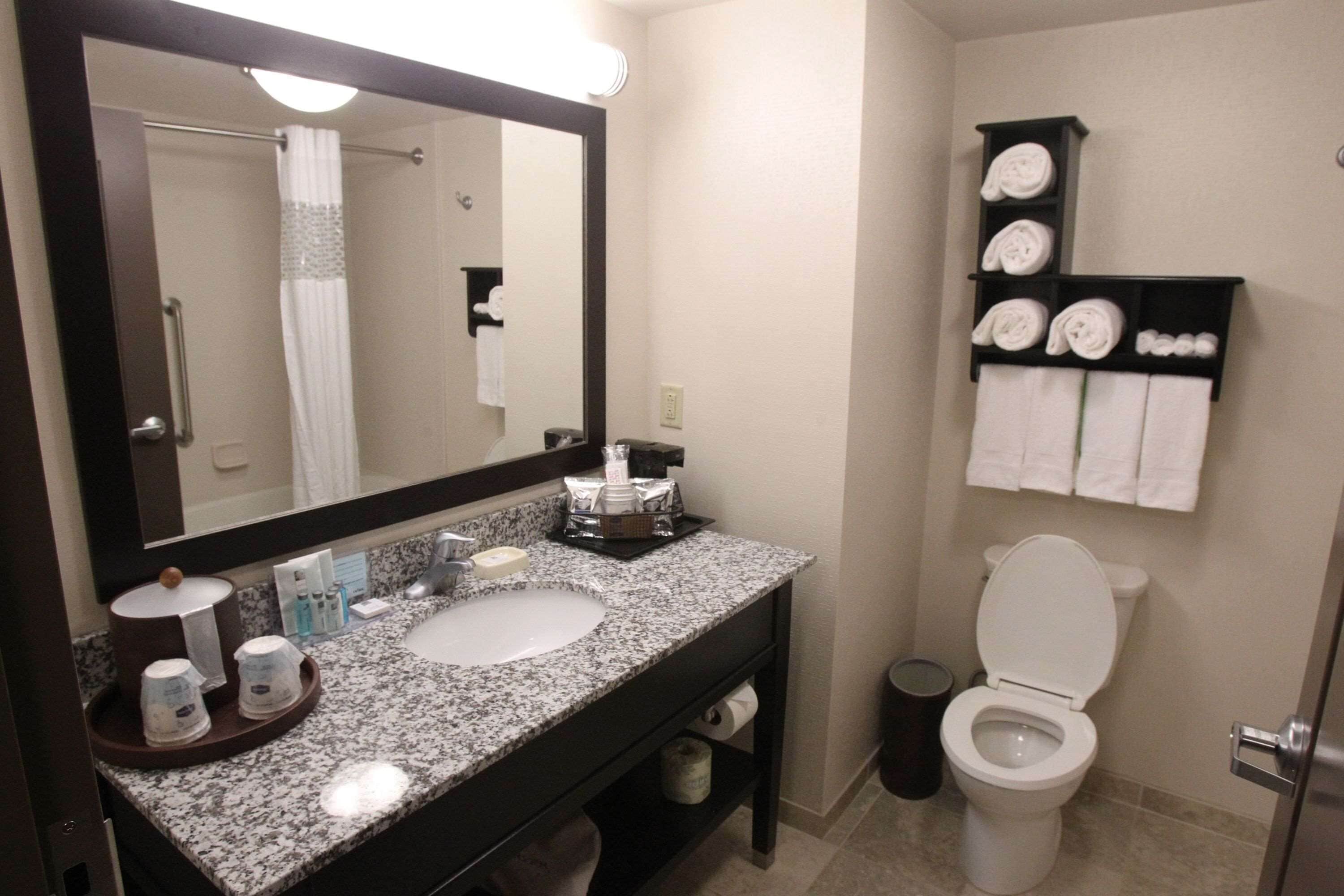 A bathroom with a sink, mirror, towel rack, toilet, and a trash bin.
