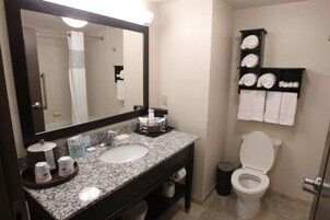 A bathroom with a sink, mirror, towel rack, toilet, and a trash bin.