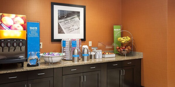 A hotel breakfast area with a coffee machine, juice dispenser, and various food items on the counter.