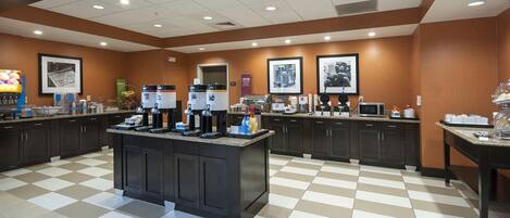 A hotel kitchen with a central island, multiple coffee machines, and a check-in counter.