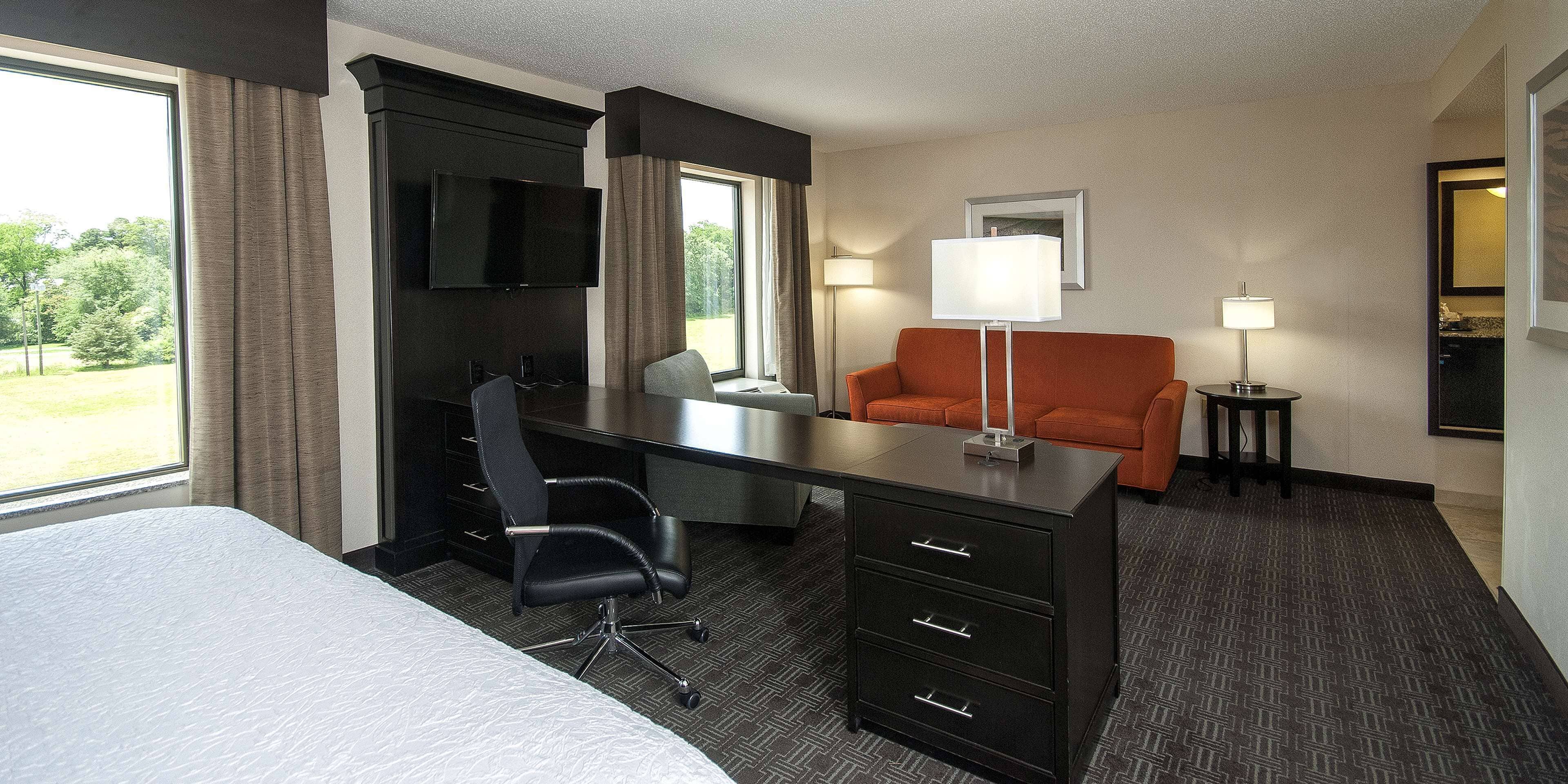 Una habitación de hotel con cama, escritorio, silla, televisión, lámpara y una mesita.