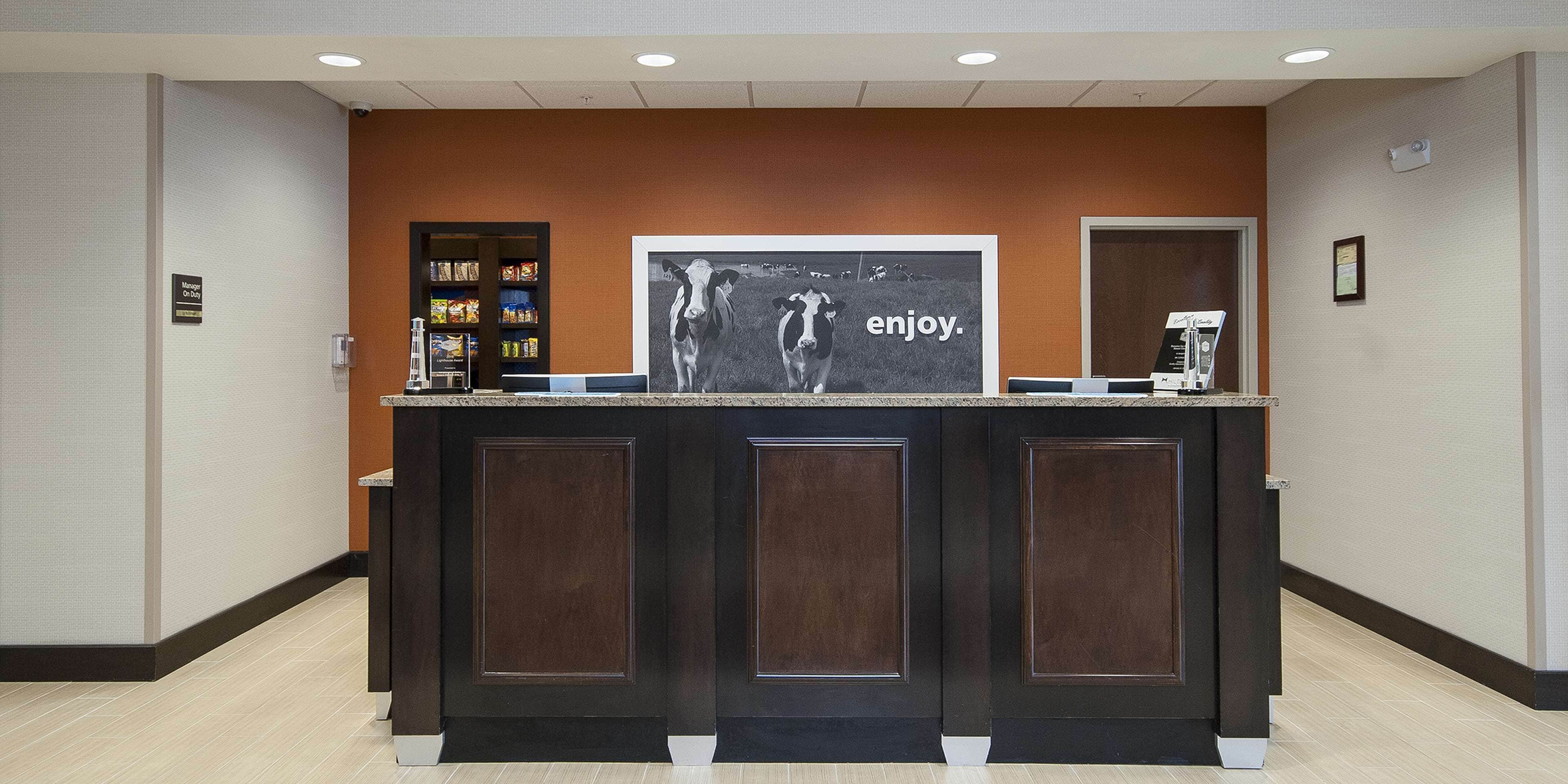 A reception desk with a framed picture of a cow and the word "enjoy." on the wall behind it.