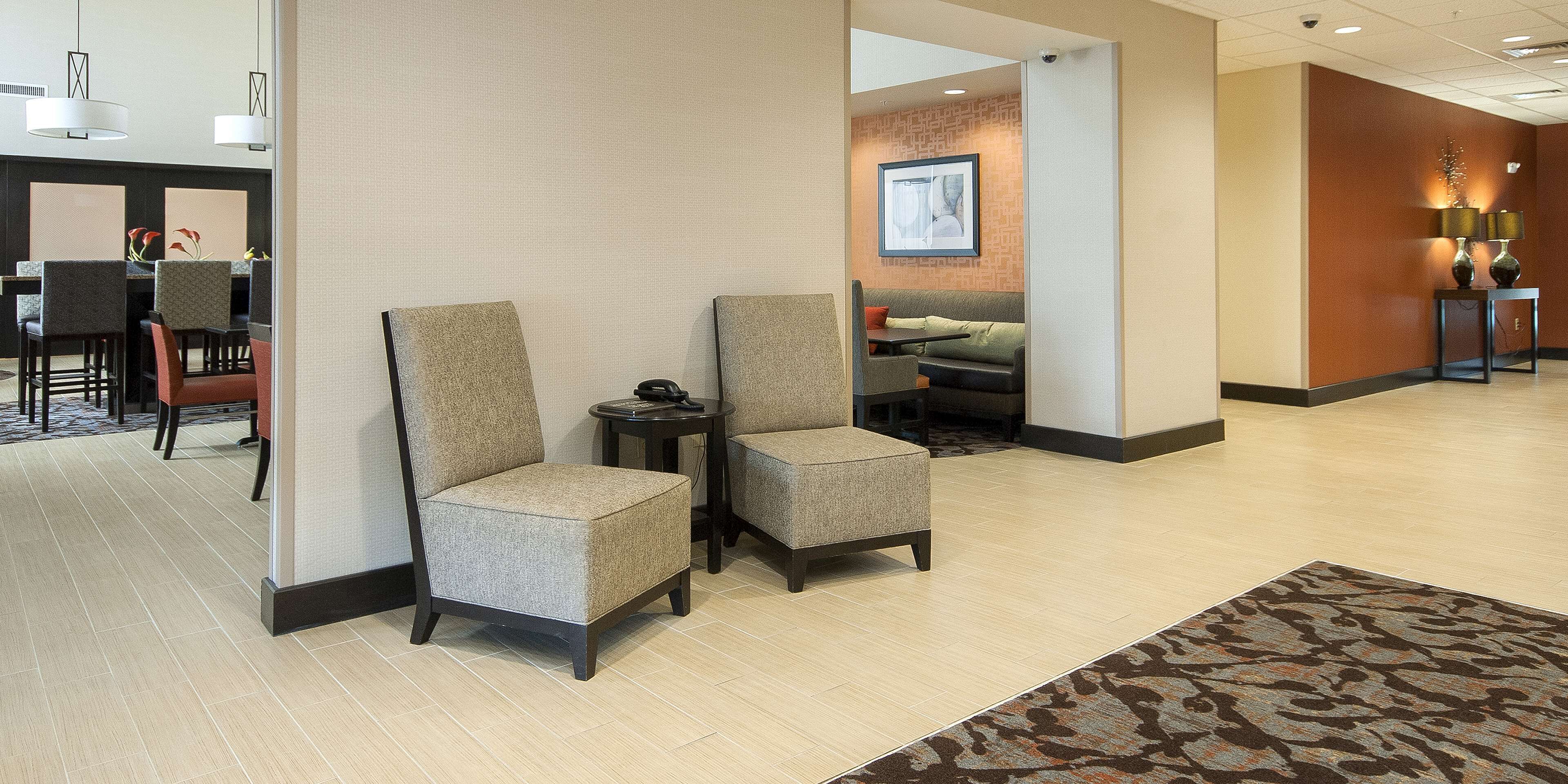 A lobby with two armchairs, a small table, and a sofa. There is a framed picture on the wall and a lamp on a side table.