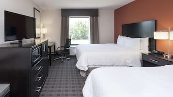 Habitación de hotel con dos camas, un escritorio, televisión y ventana con cortinas.