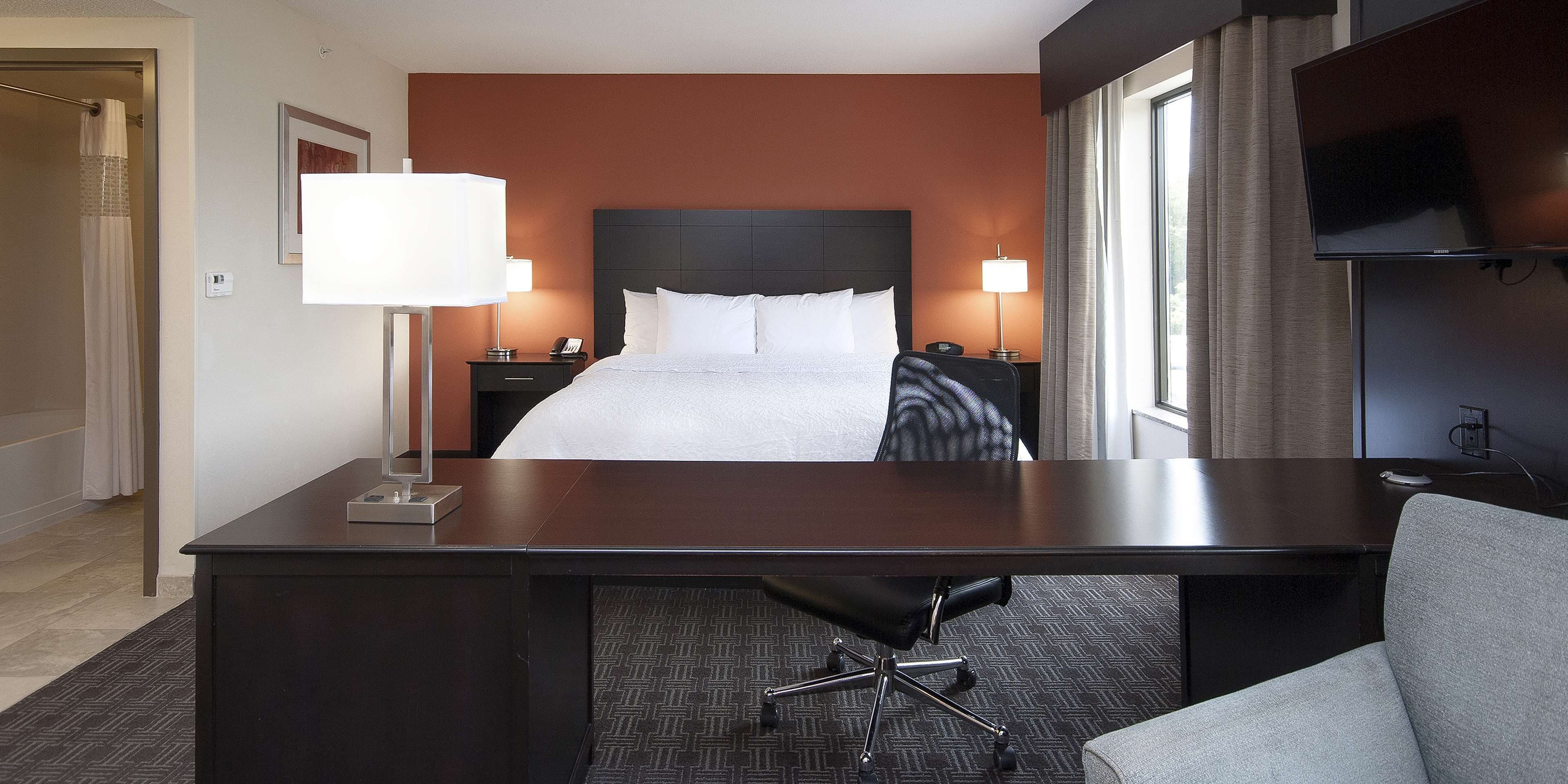 A hotel room with a bed, desk, chair, lamps, and a TV.