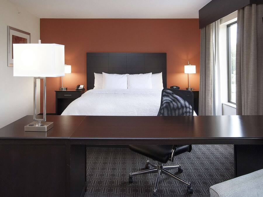 A hotel room with a bed, desk, chair, lamps, and a TV.