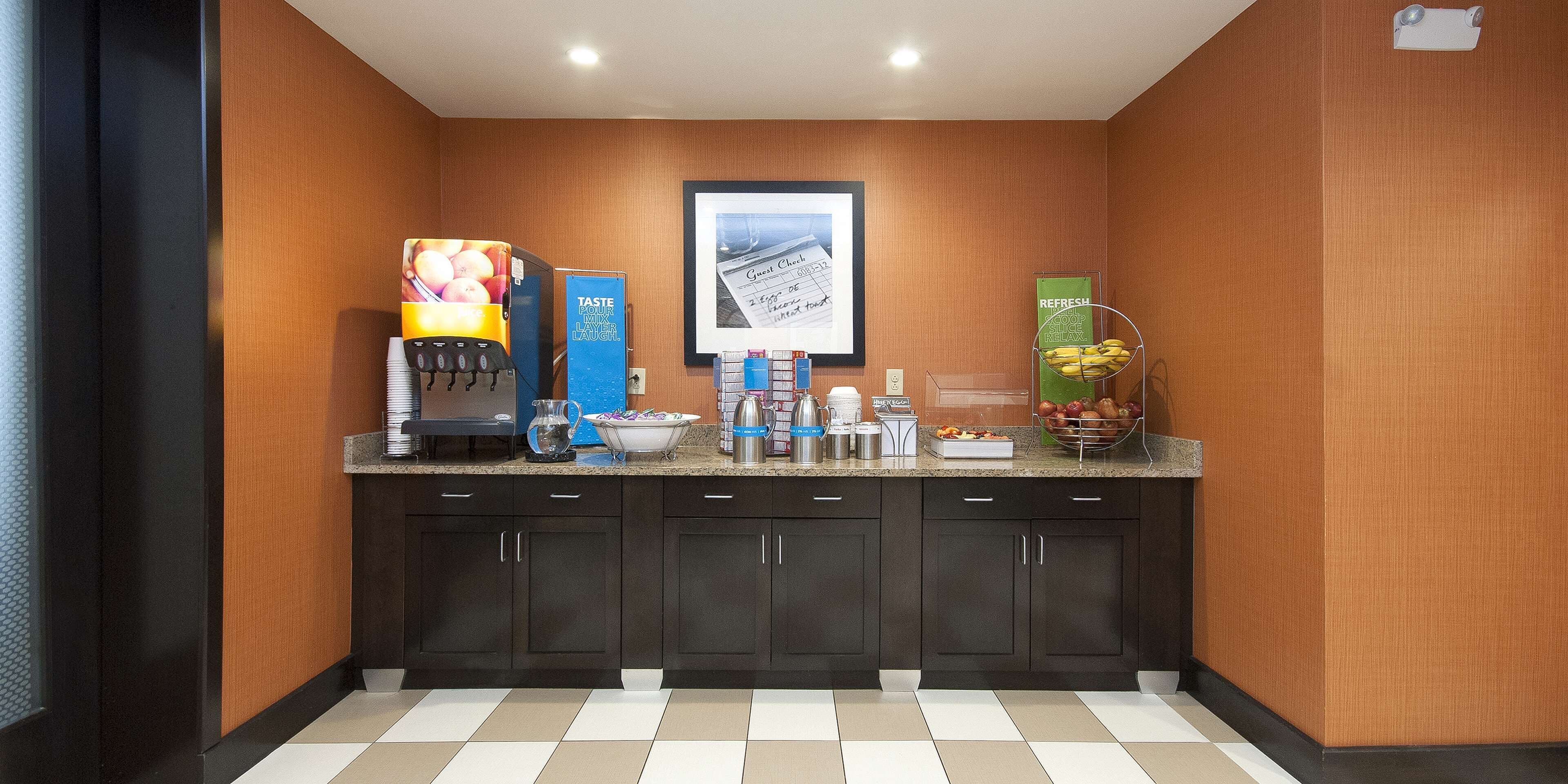 Una cocina de hotel con una cafetera, un frutero, un letrero que dice 'TASTE LAUGH' y un cuadro en la pared.