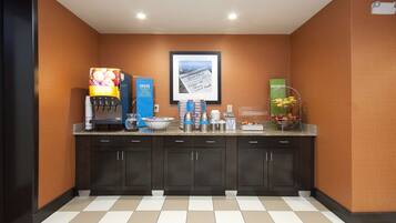 Una cocina de hotel con una cafetera, un frutero, un letrero que dice 'TASTE LAUGH' y un cuadro en la pared.