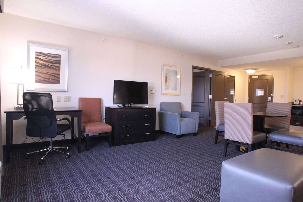 Habitació d'hotel amb escriptori, televisió, cadira, sofà i porta que dona a un bany.