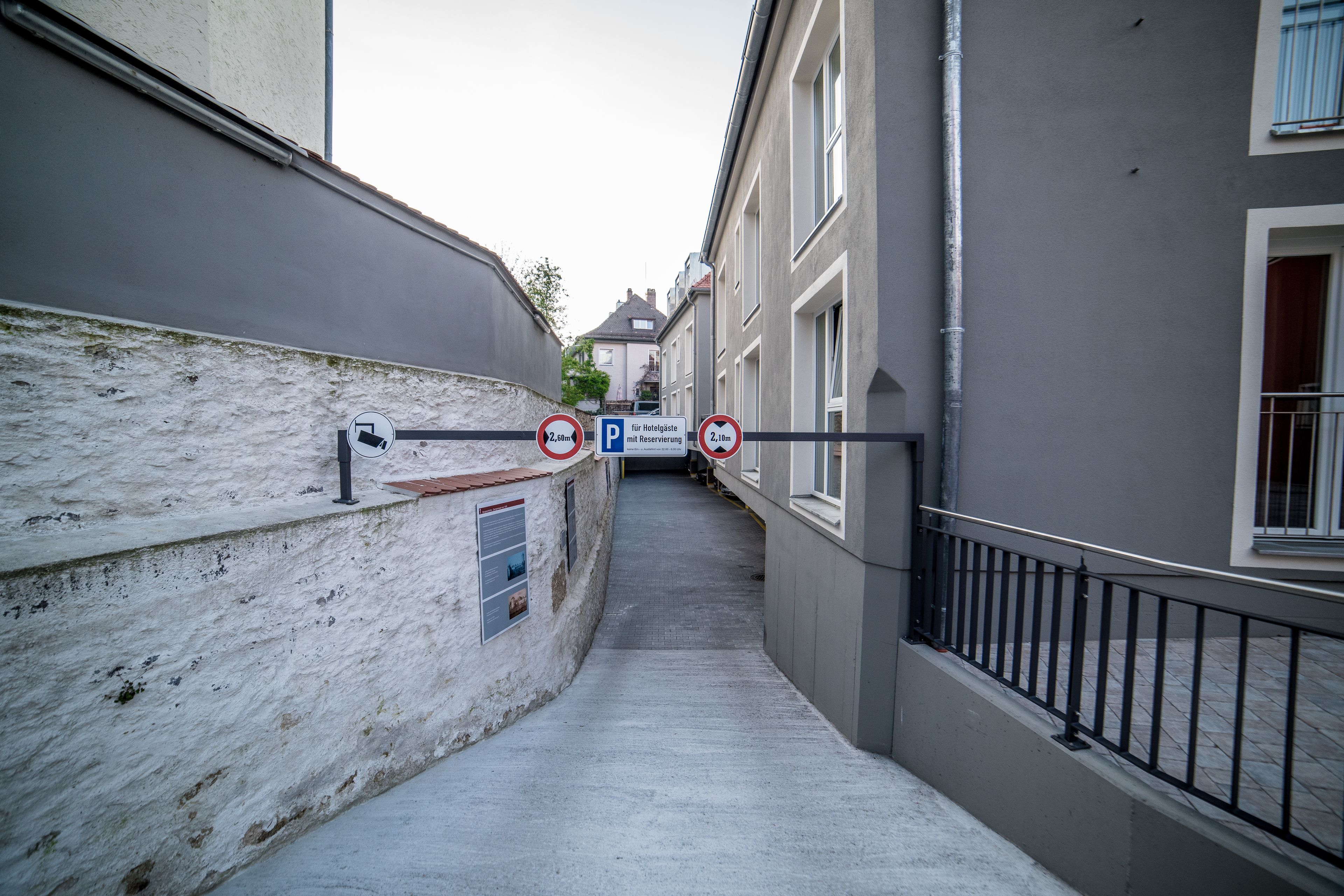 Ein schmaler Gang mit einem Parkschild, einem Gebäude mit weißer Fassade und einem Metallgeländer.
