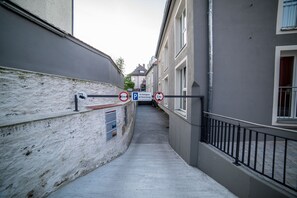 Un carreró estret amb un senyal de pàrquing, un edifici de façana blanca i una barana metàl·lica.