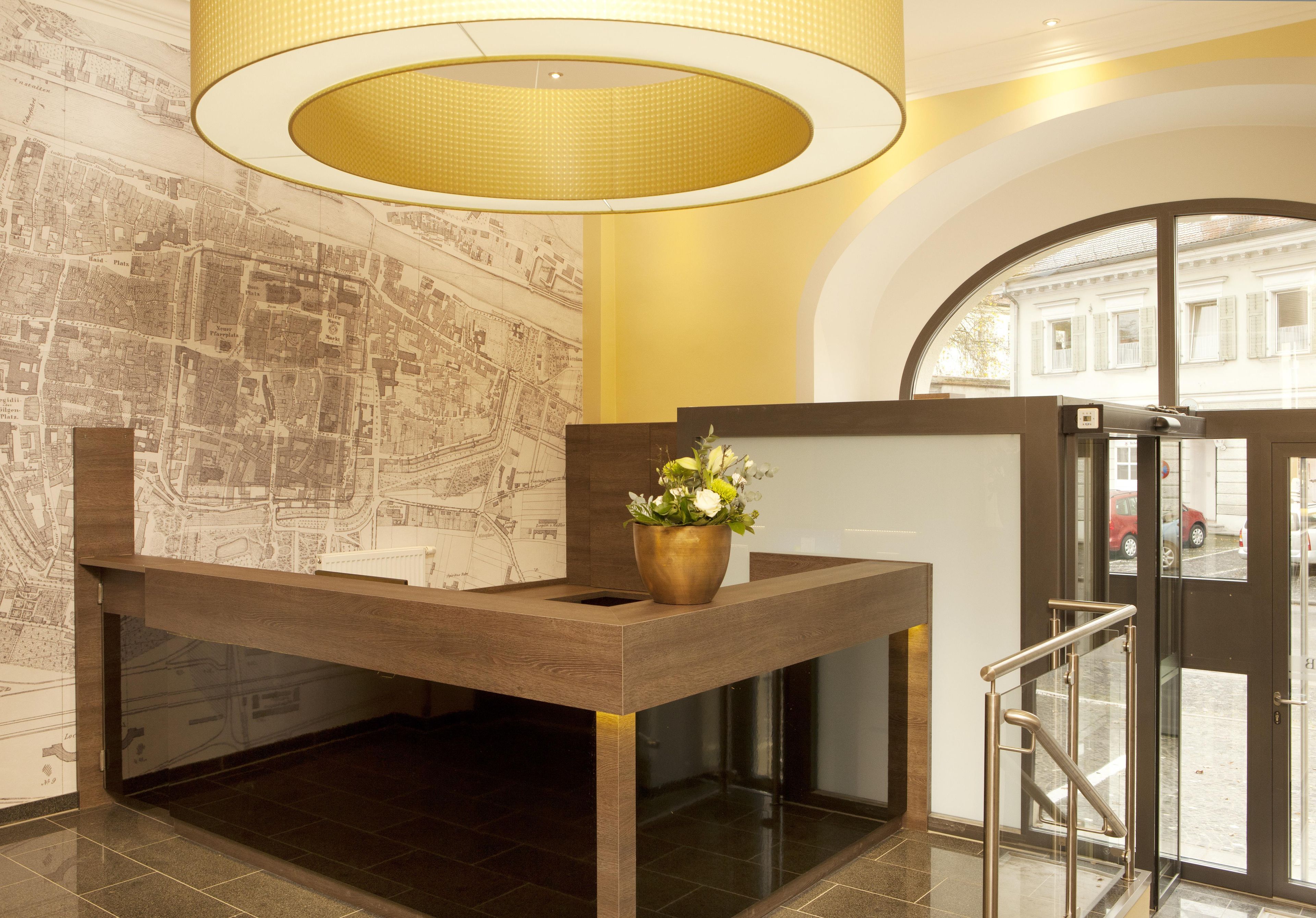 Un mostrador de recepción con un mapa, un jarrón de bronce con flores y una puerta de cristal que da al exterior.