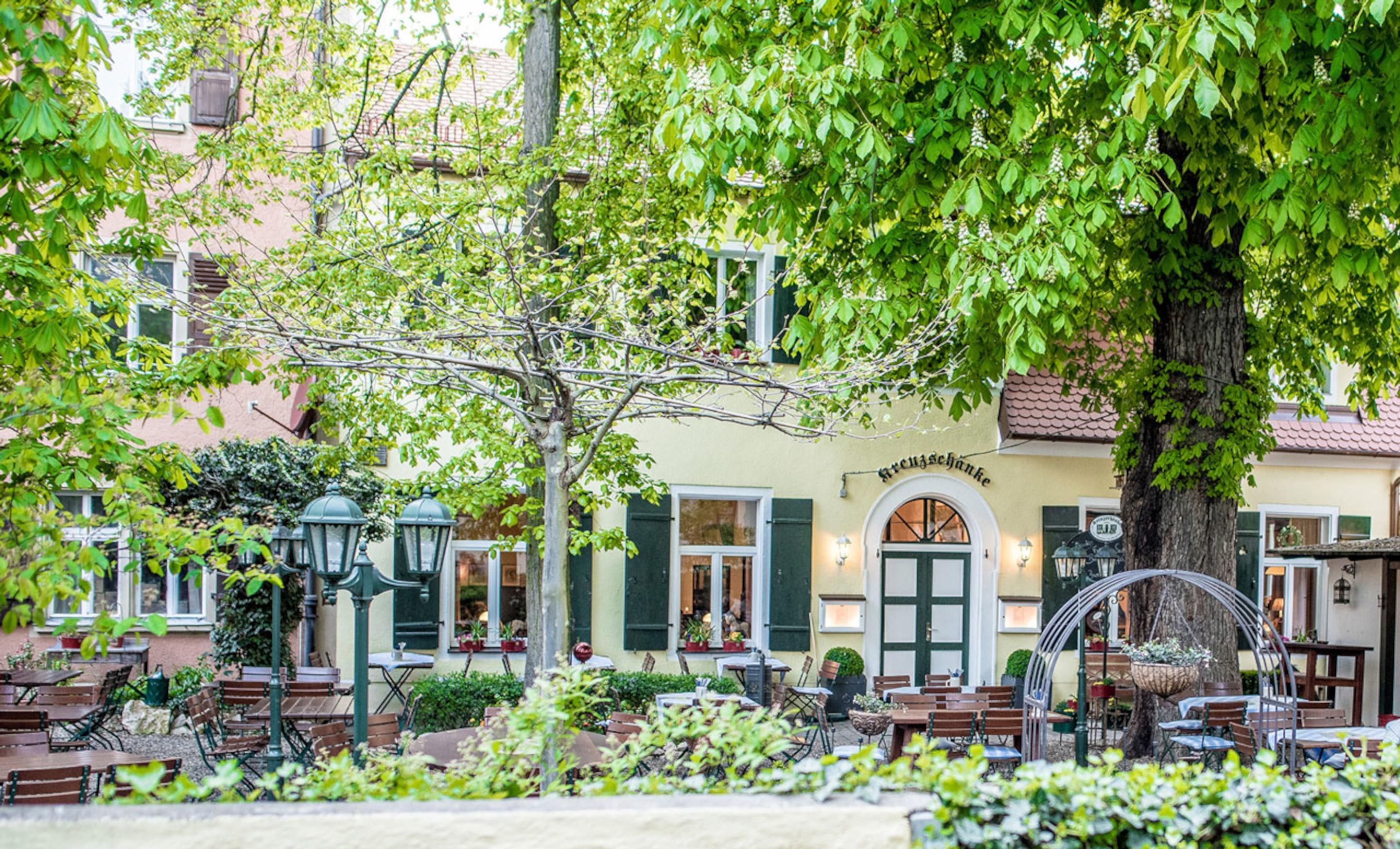Un café al aire libre con mesas y sillas, un árbol y un edificio con un letrero.