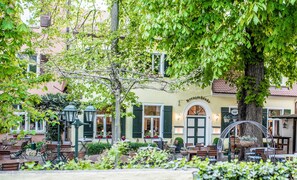 Un café en plein air avec des tables et des chaises, un arbre et un bâtiment portant une enseigne.