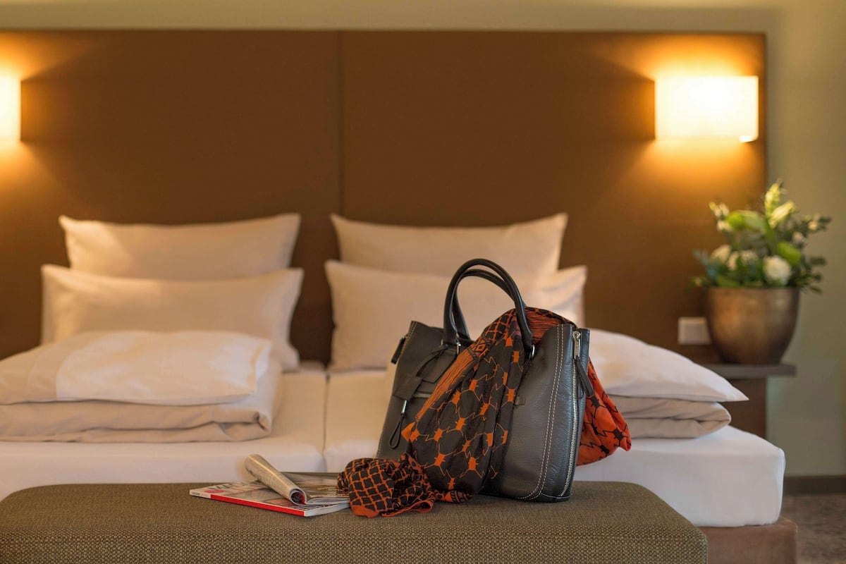 A neatly made bed with pillows, a handbag, and a book on an ottoman in a hotel room.