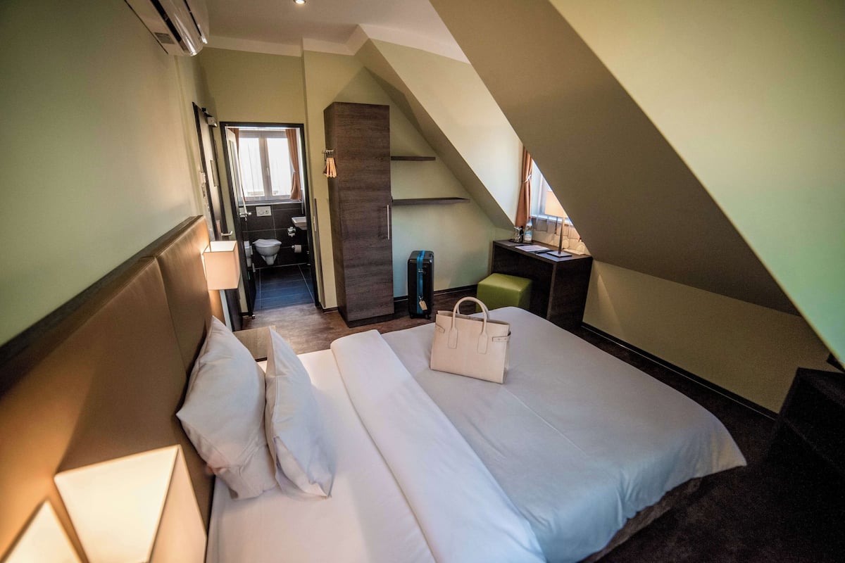 A bedroom with a large bed, a desk, a chair, and a bathroom visible through an open door.