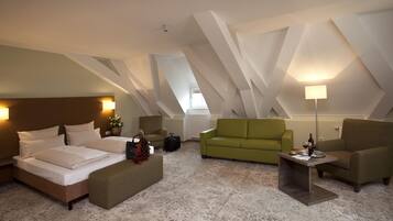A hotel room with a bed, a green sofa, a small table, and a lamp.