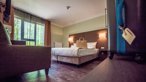 Habitación de hotel con cama, una silla, una maleta y ventana con cortinas.