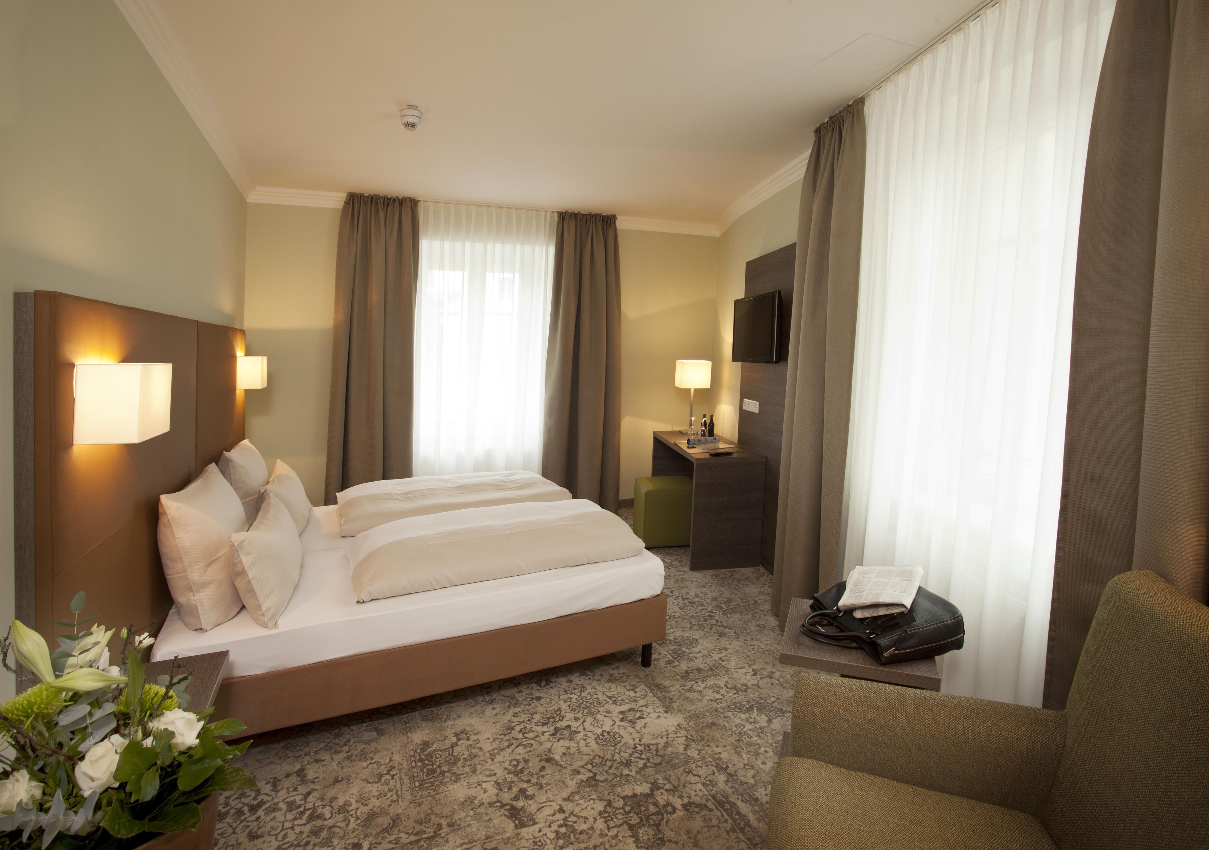A hotel room with a large bed, a desk, a chair, and a television.
