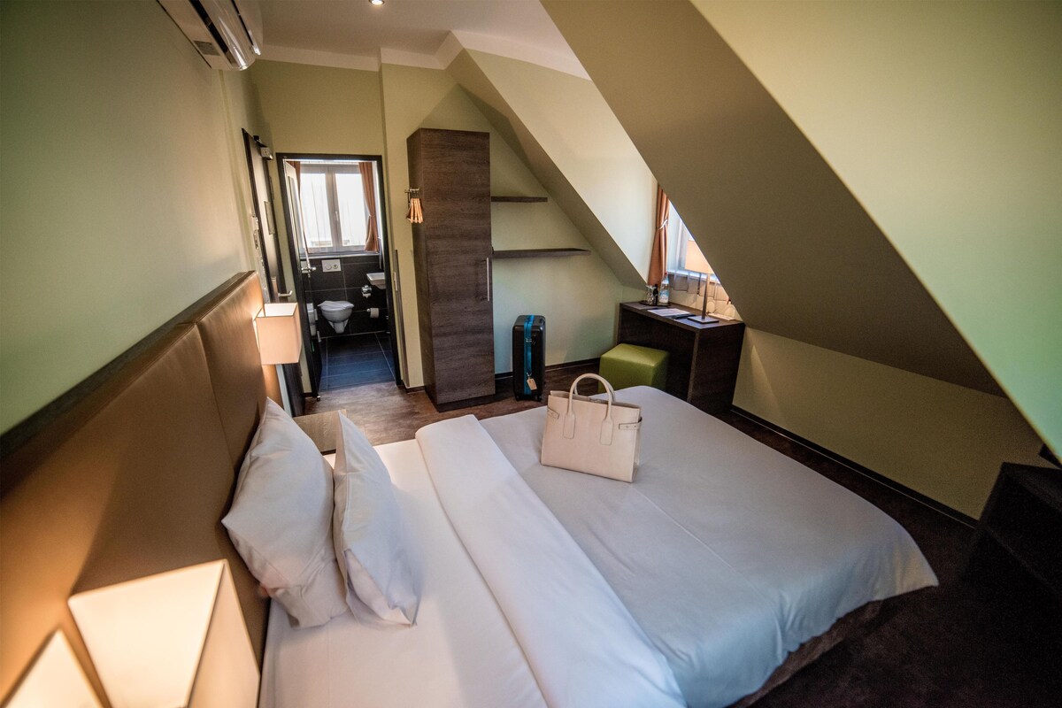 A hotel room with a bed, a desk, a chair, a bathroom, and a staircase.