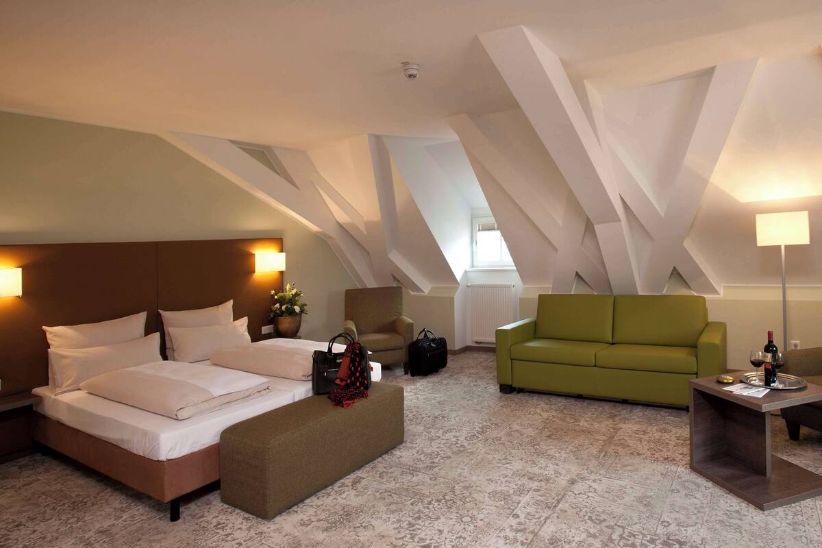 A hotel room with a bed, a green sofa, and a small table with a lamp.
