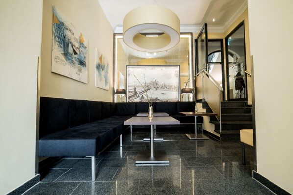 Un vestíbul modern amb un sofà negre, una taula de recepció i una escala.
