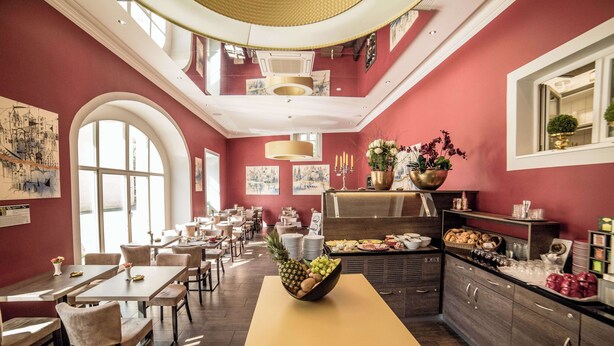 A dining area with tables, chairs, a fruit bowl, and a buffet counter with food items. - Hotel Jakob Regensburg DownTown, BW Signature Collection (Regensburg)