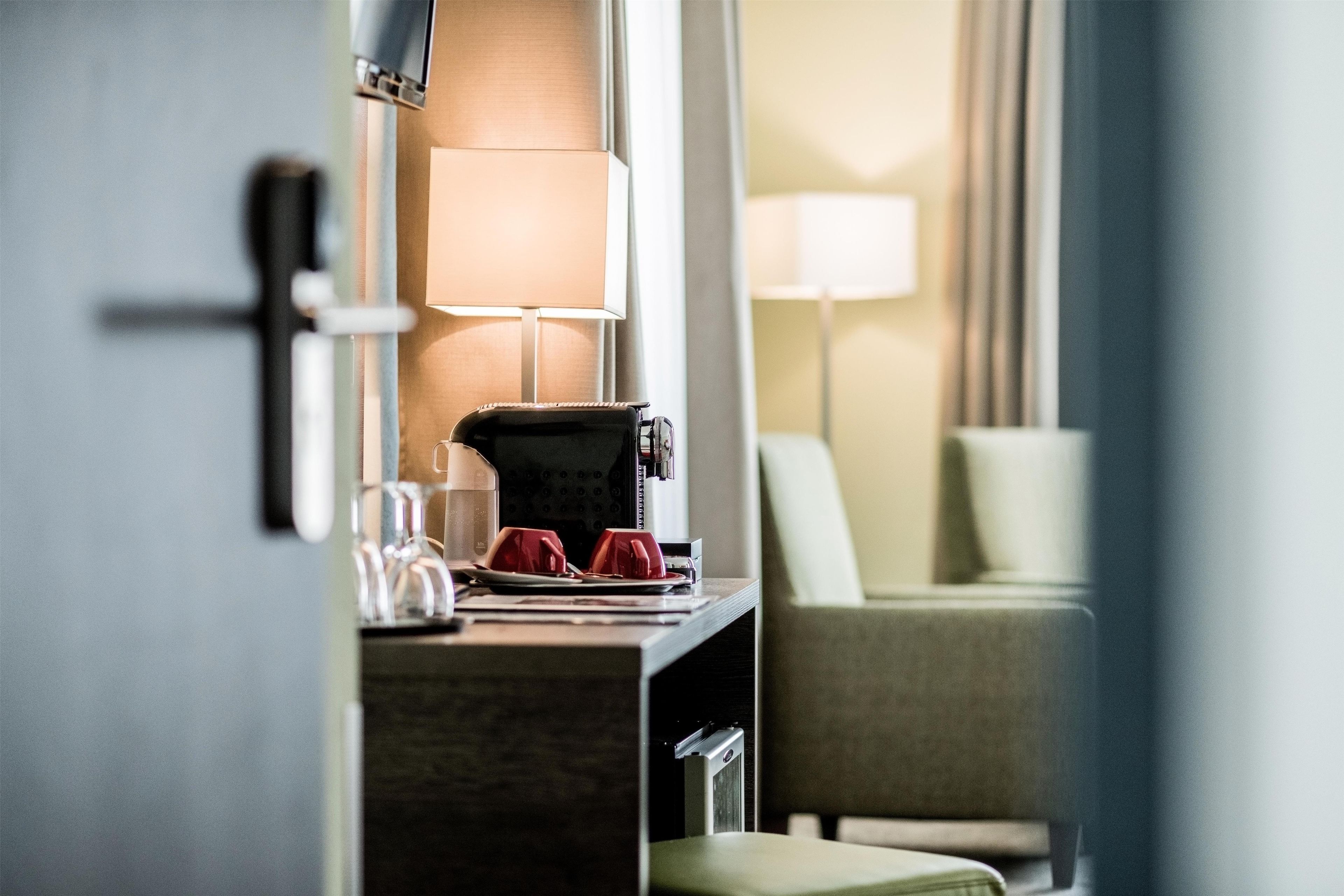 Habitació d'hotel amb escriptori, cafetera, làmpada i cadira.